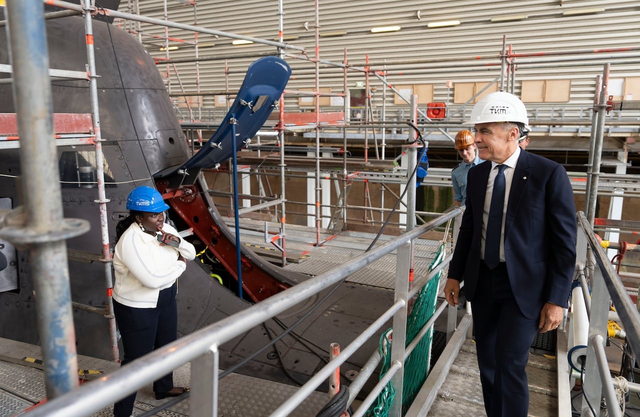 A man in a suit and a hard hat looking at a submarine propeller.